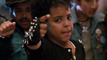 Movie still from “Moonwalker” (1988), directed by Jerry Kramer – A little boy holding a cell phone up to his ear; Close Up shot, High angle