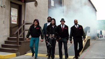 Movie still from “Moonwalker” (1988), directed by Jerry Kramer – A group of men in suits and ties standing next to each other on a sidewalk; Wide shot, Low angle