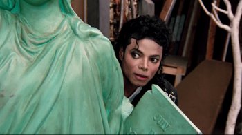 Movie still from “Moonwalker” (1988), directed by Jerry Kramer – A person with a statue in the background; Close Up shot, High angle