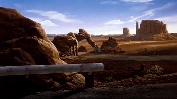 Movie still from “Moonwalker” (1988), directed by Jerry Kramer – An oil painting of a desert scene with a motorcycle rider; Extreme Wide shot, High angle