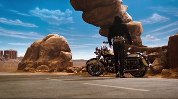 Movie still from “Moonwalker” (1988), directed by Jerry Kramer – A man standing next to a motorcycle in a parking lot; Wide shot, High angle