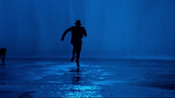 Movie still from “Moonwalker” (1988), directed by Jerry Kramer – A man in a hat running in the water; Wide shot, Low angle