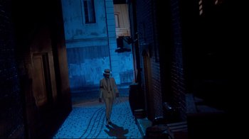 Movie still from “Moonwalker” (1988), directed by Jerry Kramer – A man walking down a street at night wearing a suit and a hat; Wide shot, High angle