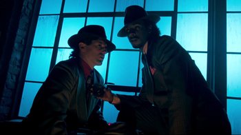 Movie still from “Moonwalker” (1988), directed by Jerry Kramer – A couple of men standing next to each other in front of a window; Medium shot, Low angle