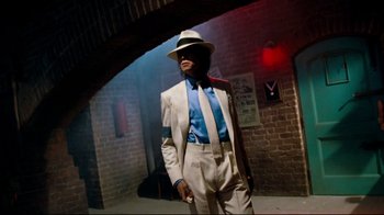 Movie still from “Moonwalker” (1988), directed by Jerry Kramer – A man in a suit and hat standing in a room; Medium shot, Low angle