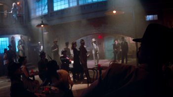 Movie still from “Moonwalker” (1988), directed by Jerry Kramer – A group of people standing around in a room; Wide shot, Over the shoulder angle