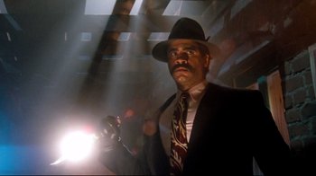 Movie still from “Moonwalker” (1988), directed by Jerry Kramer – A man in a suit and hat is holding a flashlight; Medium shot, Low angle
