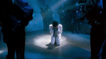 Movie still from “Moonwalker” (1988), directed by Jerry Kramer – A man kneeling down on the ground in a room; Wide shot, High angle