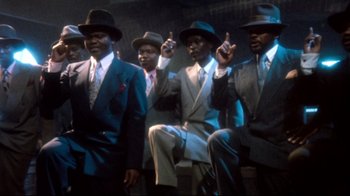 Movie still from “Moonwalker” (1988), directed by Jerry Kramer – A group of men in suits and hats are posing for a picture; Medium shot, Low angle
