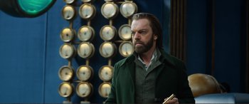 Movie still from “Mortal Engines” (2018), directed by Christian Rivers – A man with a beard is standing in front of a wall of clocks; Medium shot, Low angle