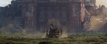 Movie still from “Mortal Engines” (2018), directed by Christian Rivers – Steam rises from a steam engine in front of an old building; Extreme Wide shot, Low angle
