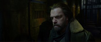 Movie still from “Mortal Engines” (2018), directed by Christian Rivers – A man with long hair and a goatee stares into the camera; Close Up shot, Over the shoulder angle