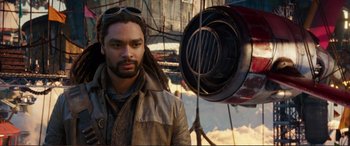 Movie still from “Mortal Engines” (2018), directed by Christian Rivers – A man with dreadlocks standing in front of an airplane; Close Up shot, Over the shoulder angle