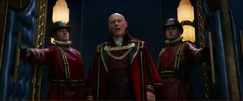 Movie still from “Mortal Engines” (2018), directed by Christian Rivers – A man in a red and black outfit standing next to two other men; Medium shot, Low angle