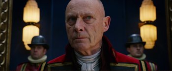 Movie still from “Mortal Engines” (2018), directed by Christian Rivers – An old man with a bald head wearing a red jacket; Close Up shot, Low angle