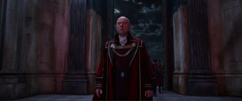 Movie still from “Mortal Engines” (2018), directed by Christian Rivers – A man in a red and black suit standing in front of a building; Medium shot, Low angle