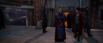 Movie still from “Mortal Engines” (2018), directed by Christian Rivers – A group of men standing next to each other on a street; Wide shot, Over the shoulder angle