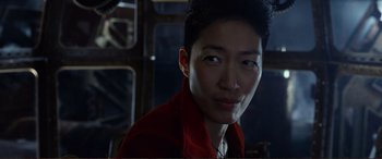 Movie still from “Mortal Engines” (2018), directed by Christian Rivers – A man in a red shirt is smiling for the camera; Close Up shot, Over the shoulder angle