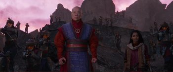 Movie still from “Mortal Engines” (2018), directed by Christian Rivers – A man in a red and blue outfit standing in front of a group of people; Medium shot, Low angle