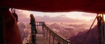 Movie still from “Mortal Engines” (2018), directed by Christian Rivers – A woman standing on top of a wooden railing looking out at the mountains; Extreme Wide shot, Low angle