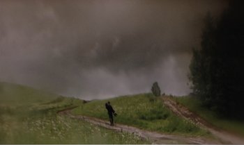 Movie still from “Mother and Son” (1997), directed by Aleksandr Sokurov – A person standing on a dirt road near a field; Extreme Wide shot, High angle