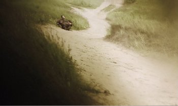 Movie still from “Mother and Son” (1997), directed by Aleksandr Sokurov – A person sitting on the ground in the grass; Extreme Wide shot, High angle