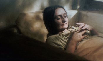 Movie still from “Mother and Son” (1997), directed by Aleksandr Sokurov – A woman sitting on a couch with her eyes closed; Close Up shot, High angle