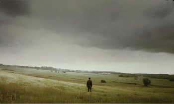 Movie still from “Mother and Son” (1997), directed by Aleksandr Sokurov – A person standing in a field under a cloudy sky; Extreme Wide shot, Low angle