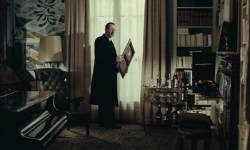 Movie still from “Mr. Klein” (1976), directed by Joseph Losey – A man in a black suit holding a picture in front of a window; Medium shot, Low angle