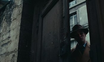 Movie still from “Mr. Klein” (1976), directed by Joseph Losey – A man wearing a hat standing in front of a door; Medium shot, Low angle
