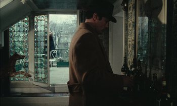 Movie still from “Mr. Klein” (1976), directed by Joseph Losey – A man standing in front of an open glass door; Medium shot, High angle