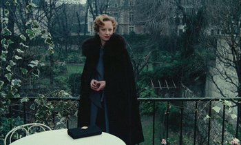 Movie still from “Mr. Klein” (1976), directed by Joseph Losey – A woman standing on a balcony holding a cell phone; Medium shot, Low angle