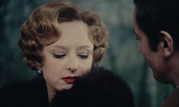 Movie still from “Mr. Klein” (1976), directed by Joseph Losey – An older woman wearing a black fur coat and red lipstick; Close Up shot, Over the shoulder angle