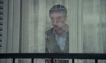 Movie still from “Mr. Klein” (1976), directed by Joseph Losey – A man looking out a window through a curtain; Medium shot, Low angle