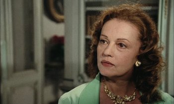 Movie still from “Mr. Klein” (1976), directed by Joseph Losey – An older woman wearing a green jacket and a gold necklace; Close Up shot, Over the shoulder angle