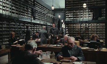 Movie still from “Mr. Klein” (1976), directed by Joseph Losey – A group of men sitting at a table in a room; Wide shot, High angle