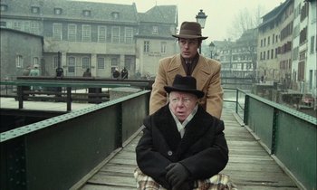 Movie still from “Mr. Klein” (1976), directed by Joseph Losey – A man sitting on the shoulders of another man on a pier; Medium shot, High angle