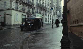 Movie still from “Mr. Klein” (1976), directed by Joseph Losey – An old car driving down a street in the rain; Extreme Wide shot, High angle