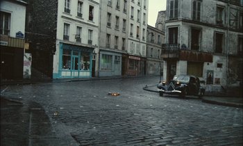 Movie still from “Mr. Klein” (1976), directed by Joseph Losey – An empty street with a car parked on the side of the road; Extreme Wide shot, High angle