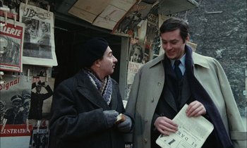 Movie still from “Mr. Klein” (1976), directed by Joseph Losey – Two men are standing together and one is holding a newspaper; Medium shot, Over the shoulder angle