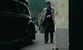Movie still from “Mr. Klein” (1976), directed by Joseph Losey – A man walking down the street with a car in the background; Medium shot, Over the shoulder angle