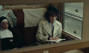 Movie still from “Mr. Klein” (1976), directed by Joseph Losey – A woman sitting on a train reading a book; Medium shot, Over the shoulder angle