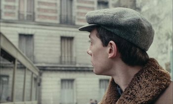 Movie still from “Mr. Klein” (1976), directed by Joseph Losey – A young man wearing a hat and a fur coat; Close Up shot, Over the shoulder angle