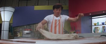 Movie still from “Mr. Nice Guy” (1997), directed by Sammo Kam-Bo Hung – A man wearing an apron is kneading dough on a table; Medium shot, Low angle