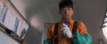 Movie still from “Mr. Nice Guy” (1997), directed by Sammo Kam-Bo Hung – A man in an orange shirt holding a blue tie; Close Up shot, Low angle