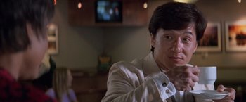 Movie still from “Mr. Nice Guy” (1997), directed by Sammo Kam-Bo Hung – A man in a white suit is holding a remote control; Close Up shot, Over the shoulder angle