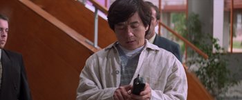 Movie still from “Mr. Nice Guy” (1997), directed by Sammo Kam-Bo Hung – A man looking at a cell phone while standing in front of a staircase; Close Up shot, Low angle
