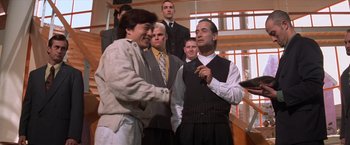 Movie still from “Mr. Nice Guy” (1997), directed by Sammo Kam-Bo Hung – A group of men standing around each other in front of a building; Medium shot, Over the shoulder angle