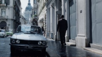 Movie still from “Munich” (2005), directed by Steven Spielberg – A man walking down the street in a suit and hat; Wide shot, Low angle