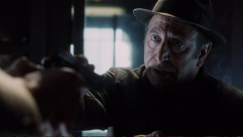 Movie still from “Munich” (2005), directed by Steven Spielberg – An older man wearing a hat is holding a pen; Close Up shot, Over the shoulder angle